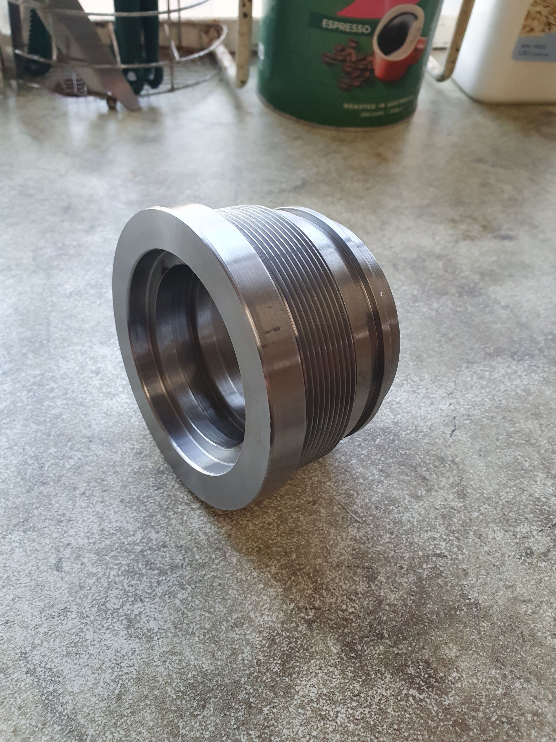 Metal threaded cylindrical component on a tabletop, silver with a knurled center section.