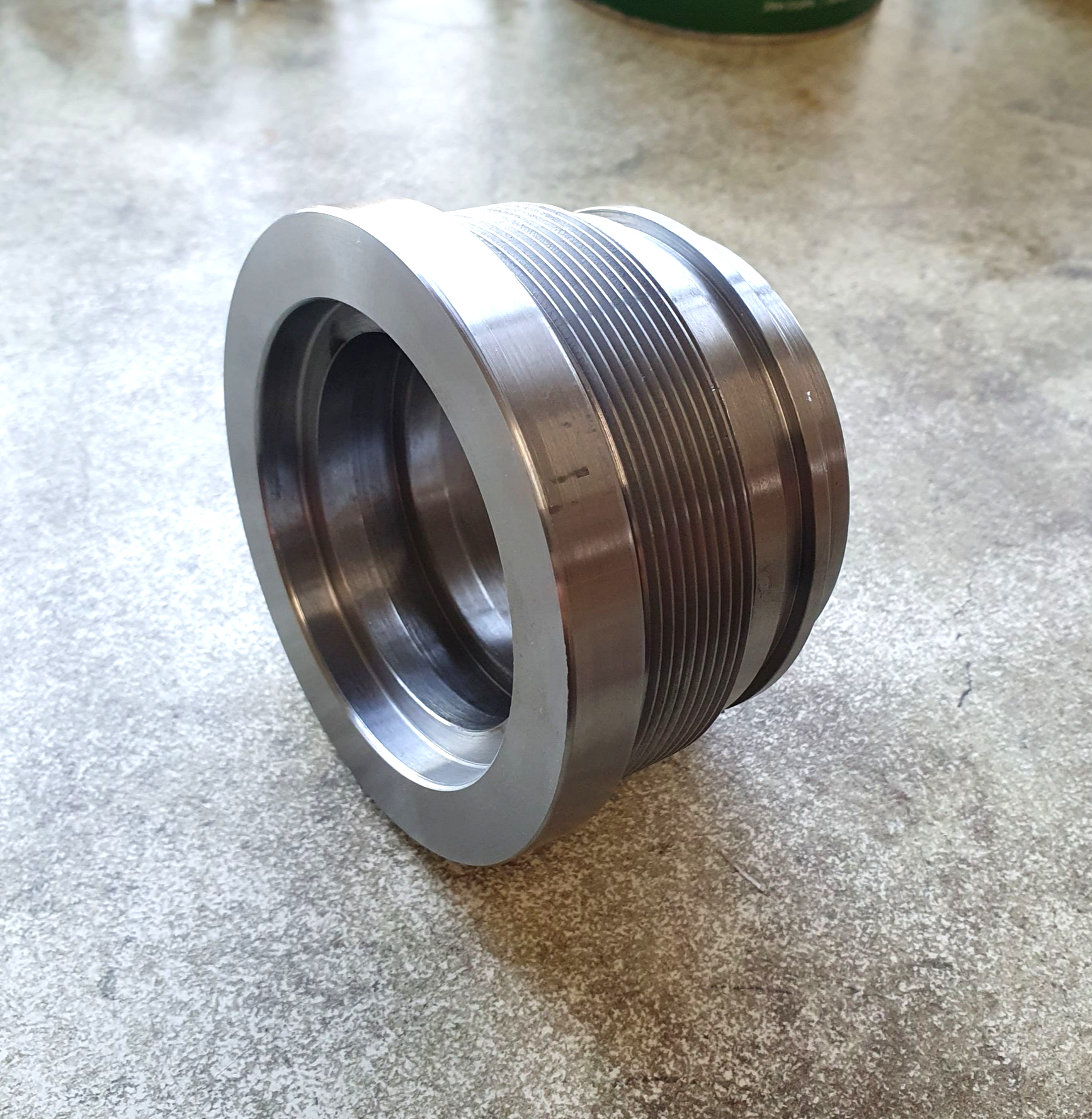 Metal threaded cylindrical component on a tabletop, silver with a knurled center section.