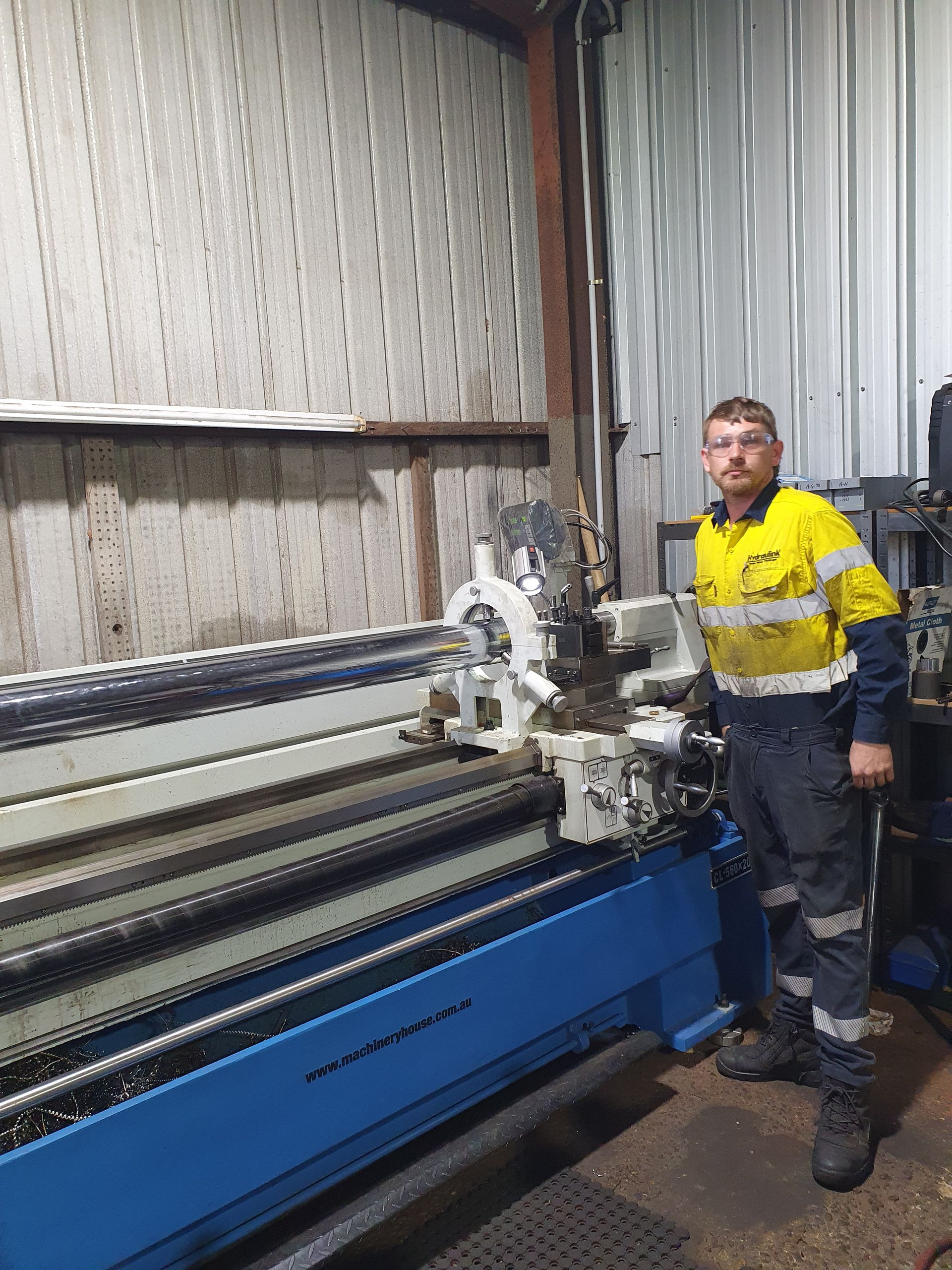 Worker in yellow safety gear standing by a large blue industrial machine in a factory.
