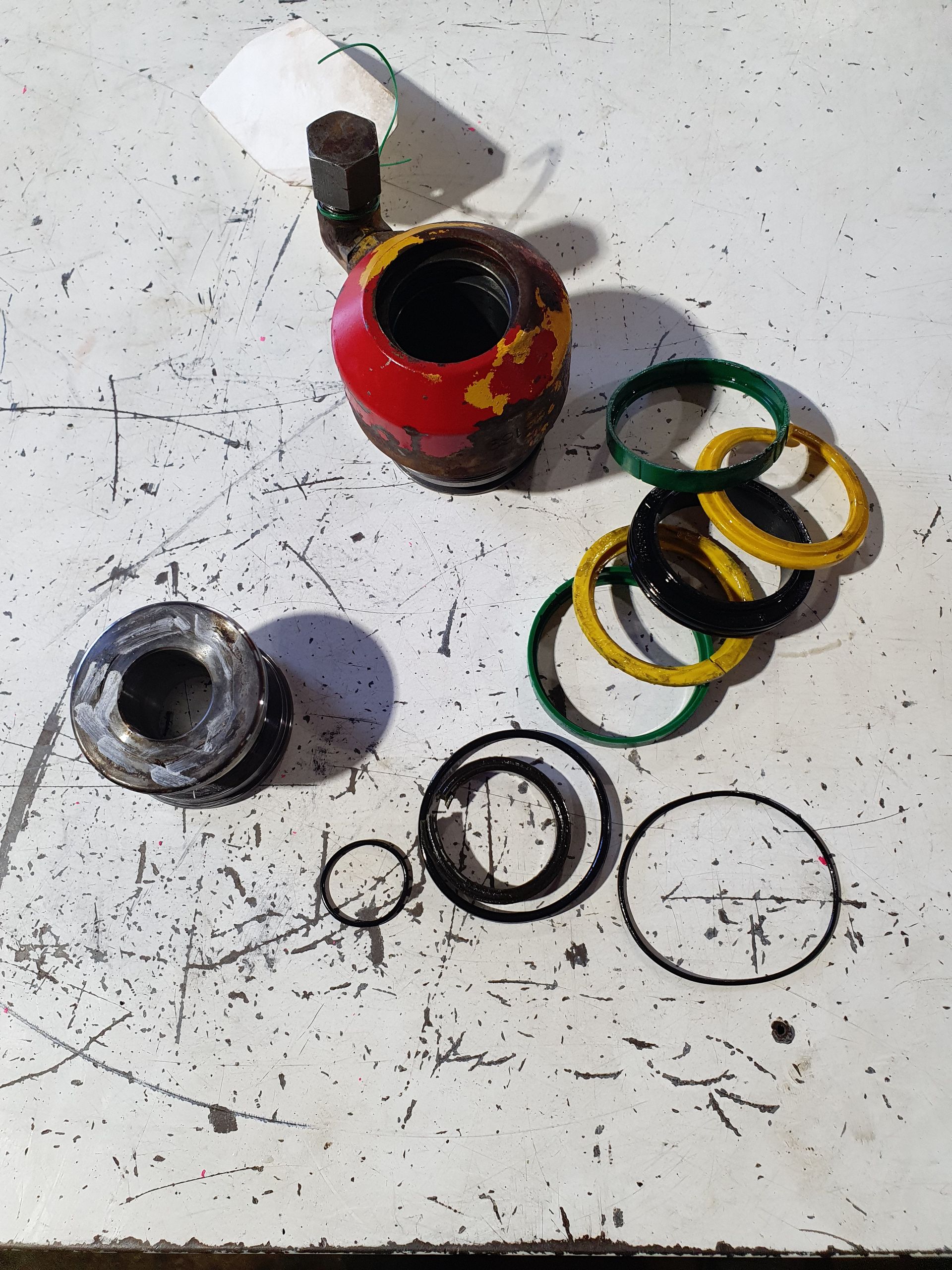 Scattered metal and rubber rings, washers, and a red cylindrical part on a white tabletop