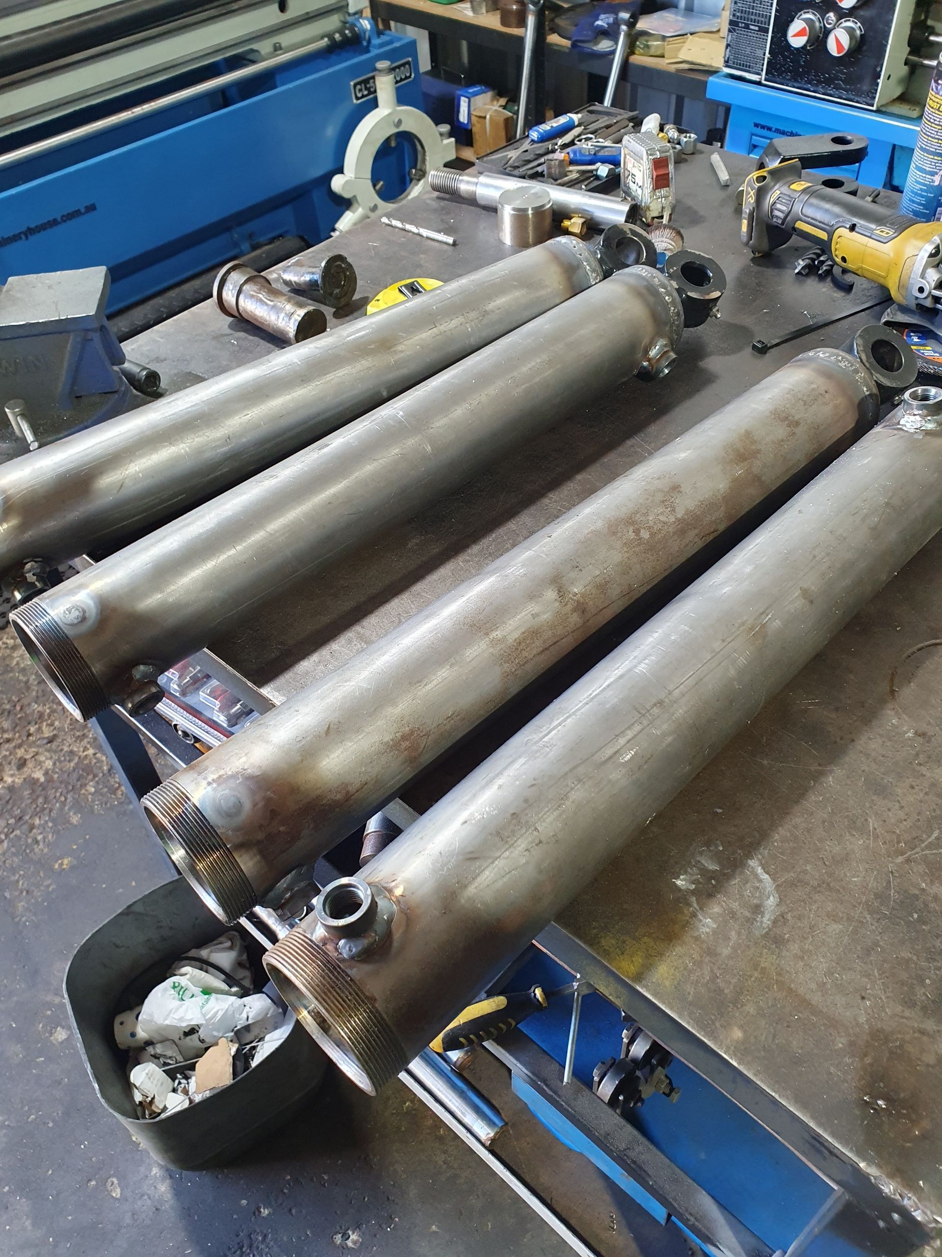 Three metal rollers on a factory machine with blue frame and scattered parts on the floor