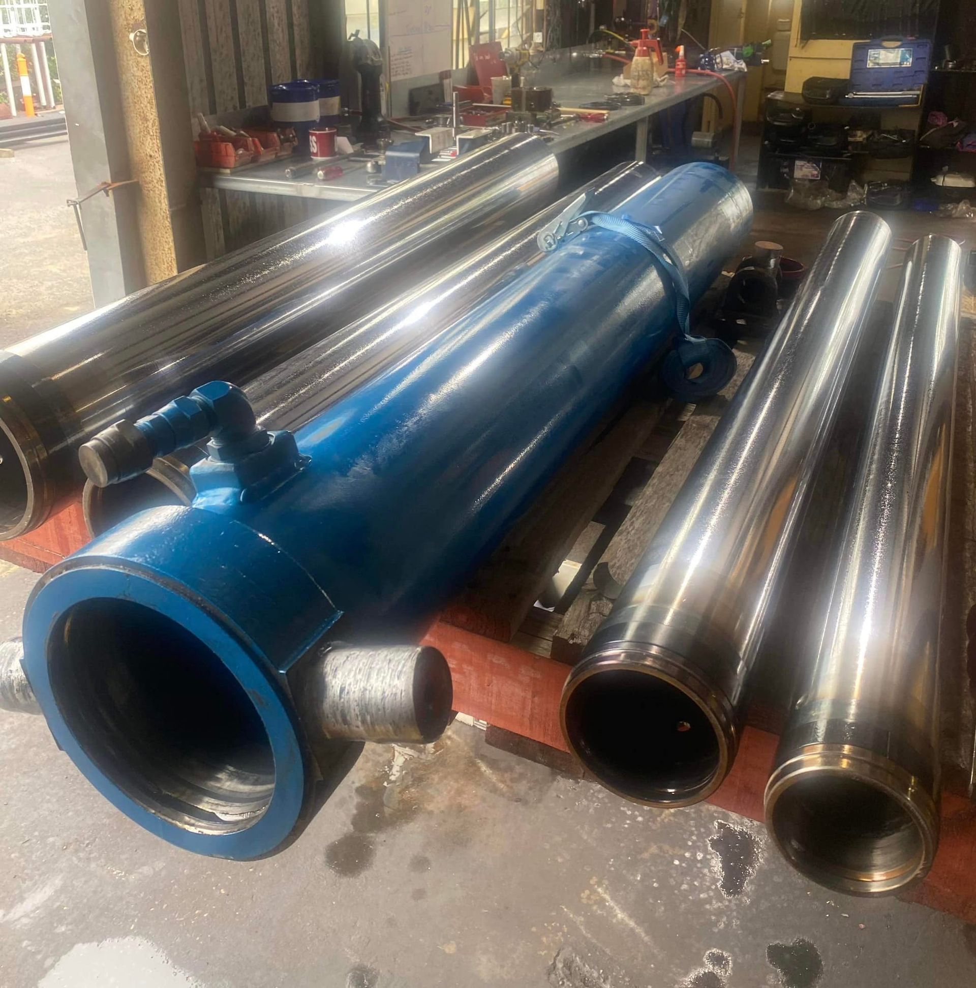 Blue industrial cylinder beside stacked shiny metal pipes in a workshop