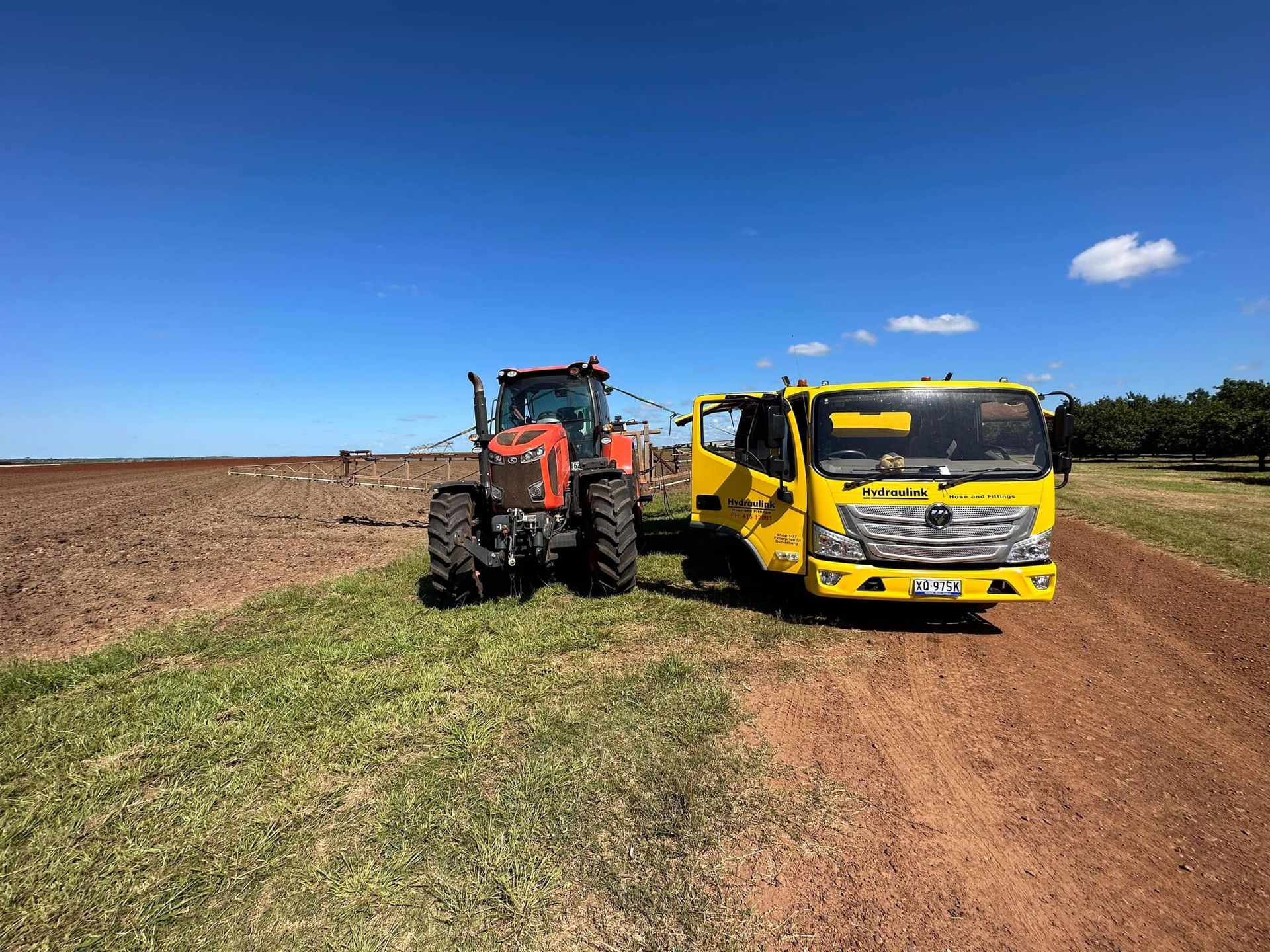 Orange tractor and yellow truck parked on a dirt field under a clear blue sky.