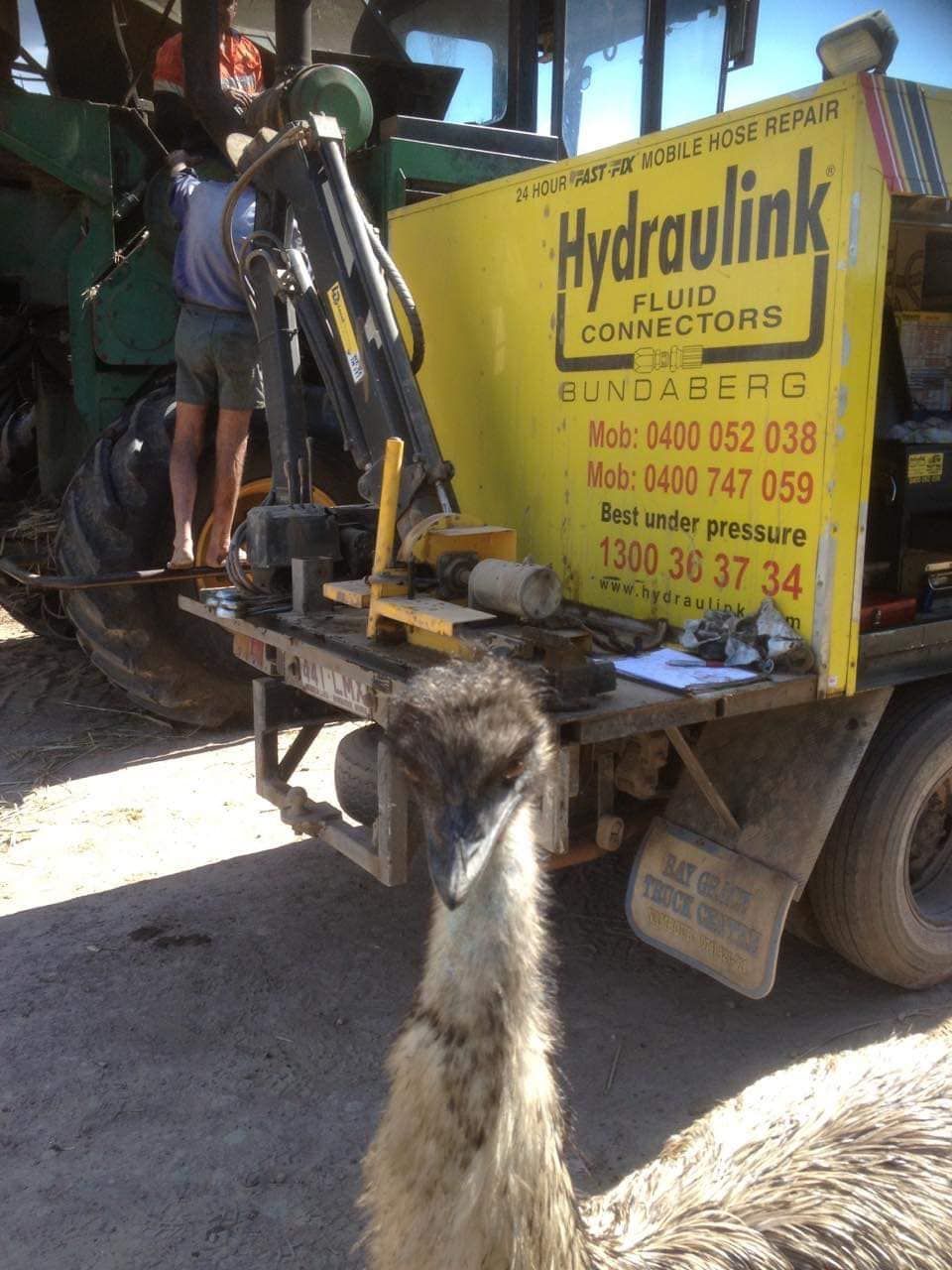 Yellow Hydraulink truck with a worker operating hydraulic equipment on a sunny roadside.