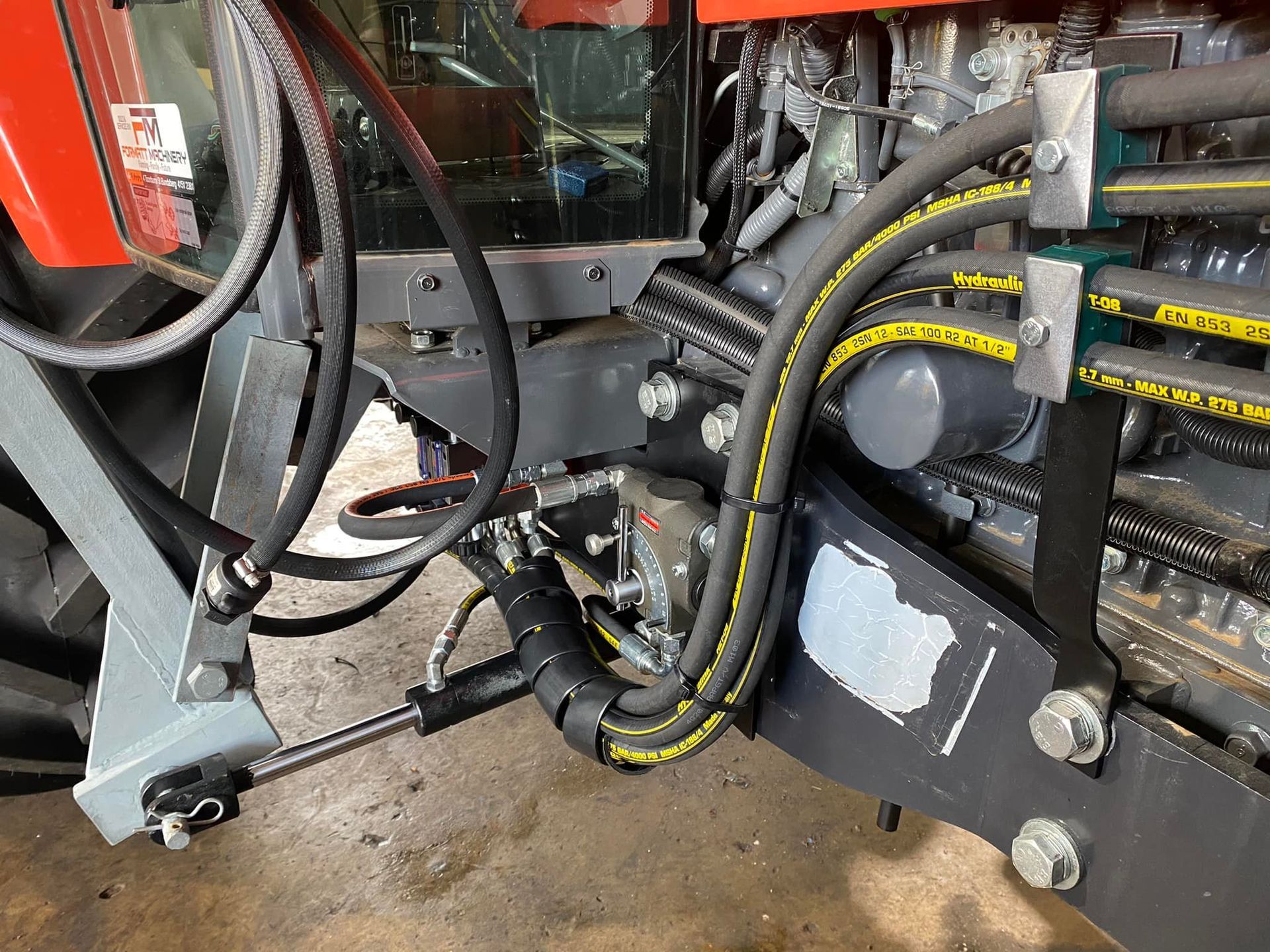 Close-up of industrial machinery with black hoses, yellow-striped cables, and metal components on a concrete floor