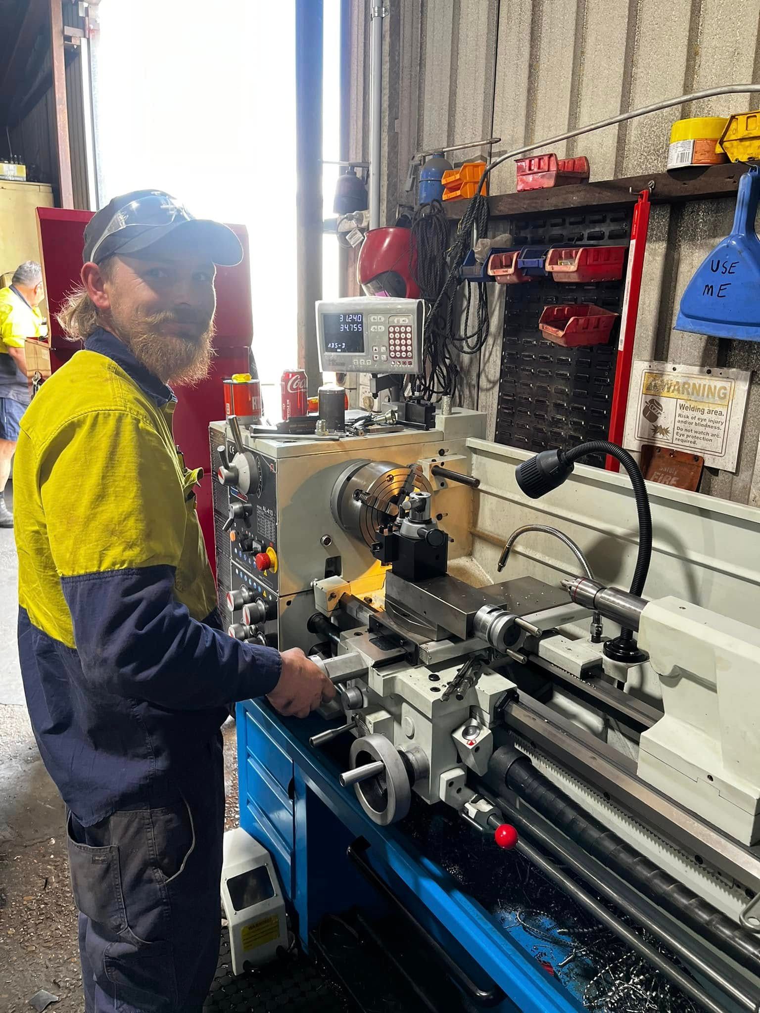 Technician in yellow and blue workwear operating a metal lathe in a workshop