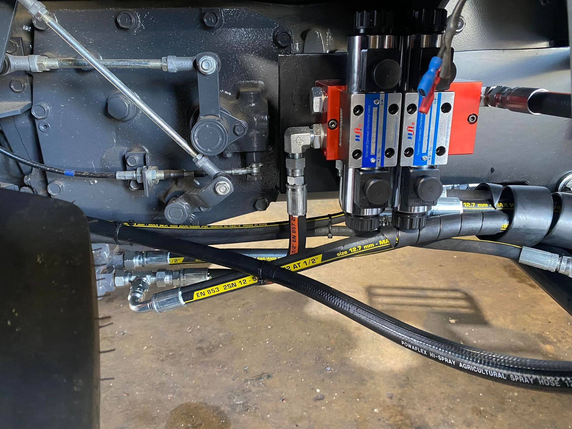 Industrial machinery with hoses, cables, and a red control lever on a metal frame indoors.