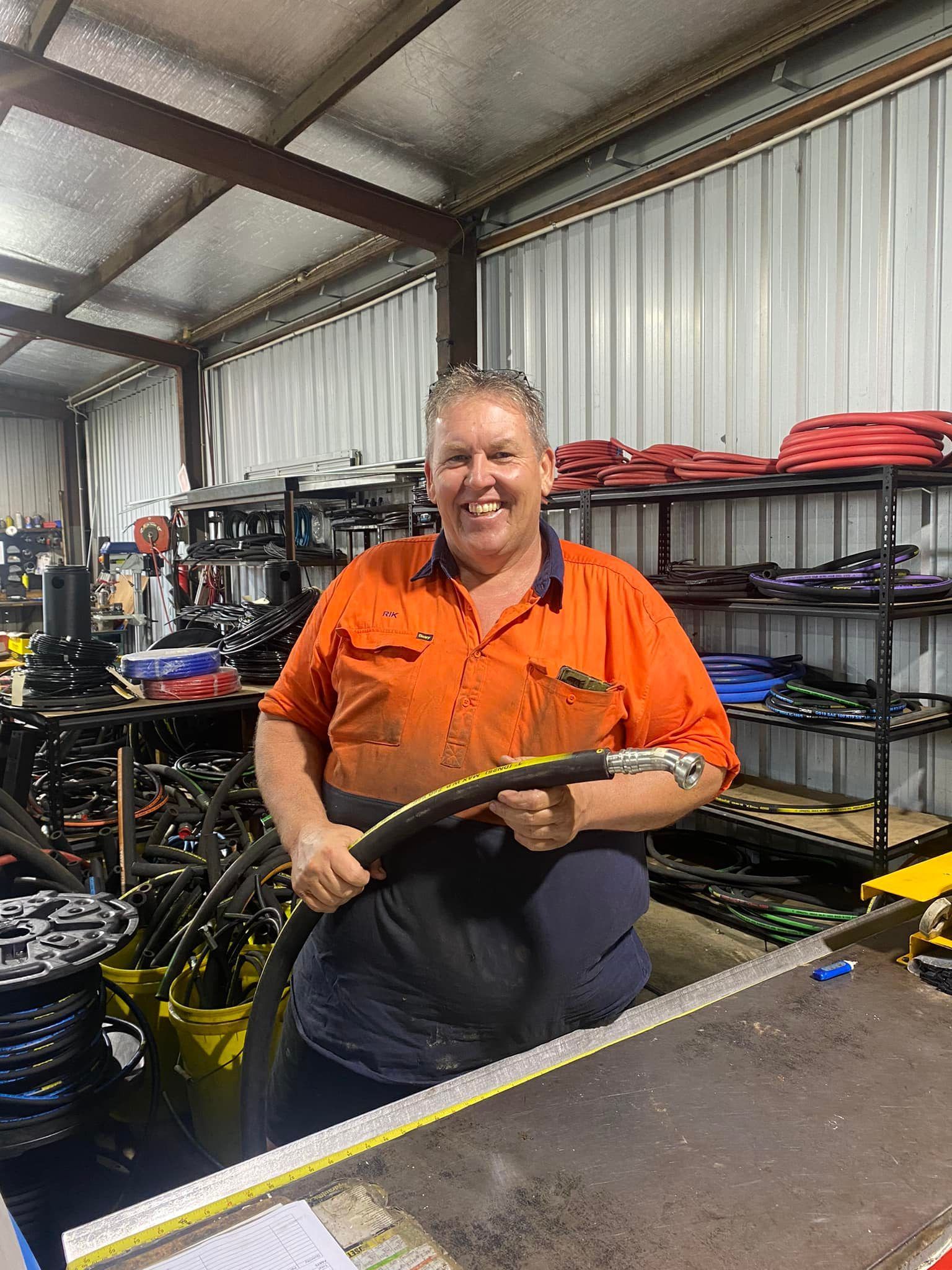 Smiling mechanic in orange shirt holding a bicycle wheel in a workshop with shelves and tools