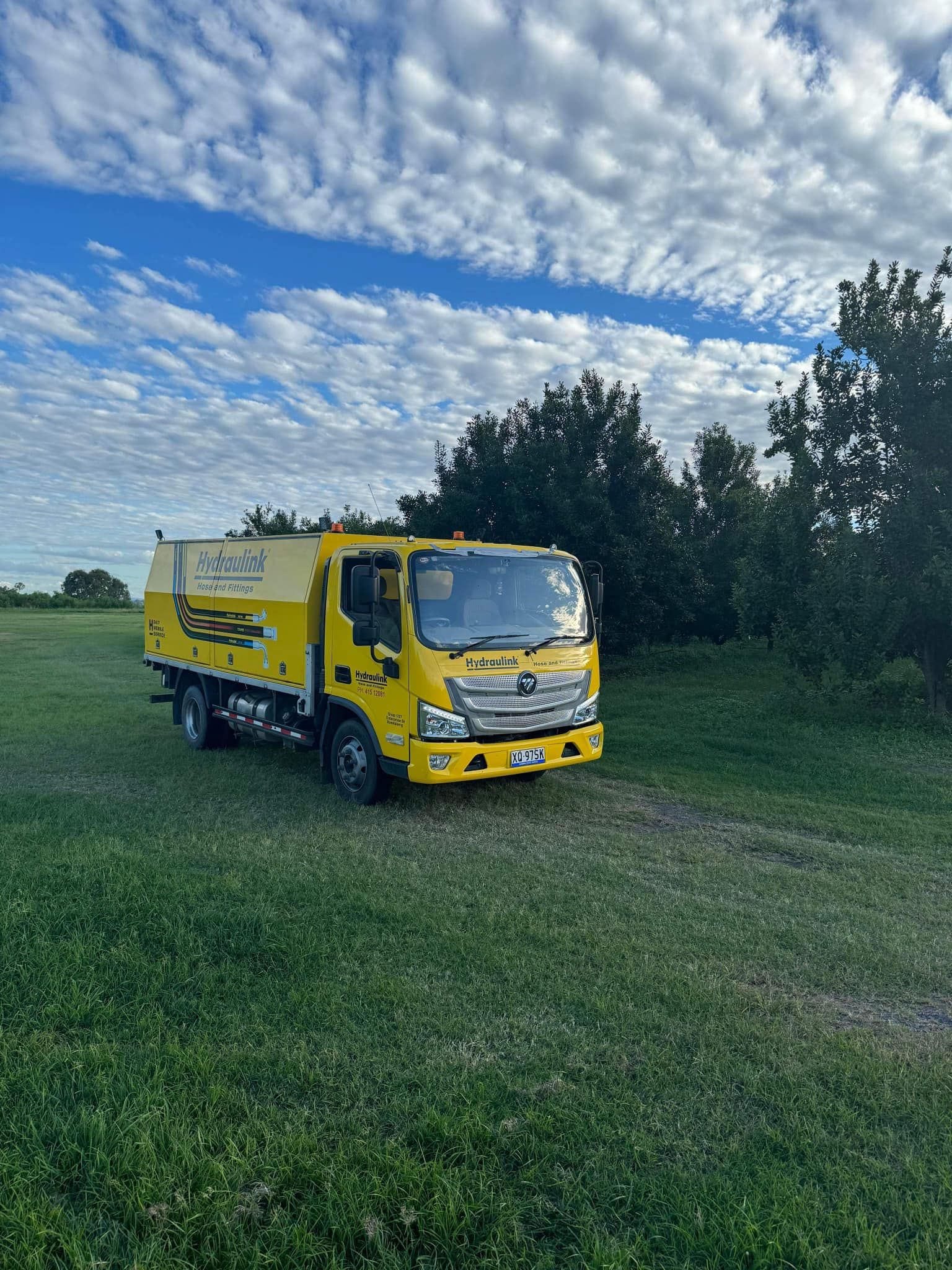 Yellow utility truck parked on grassy field under a cloudy sky