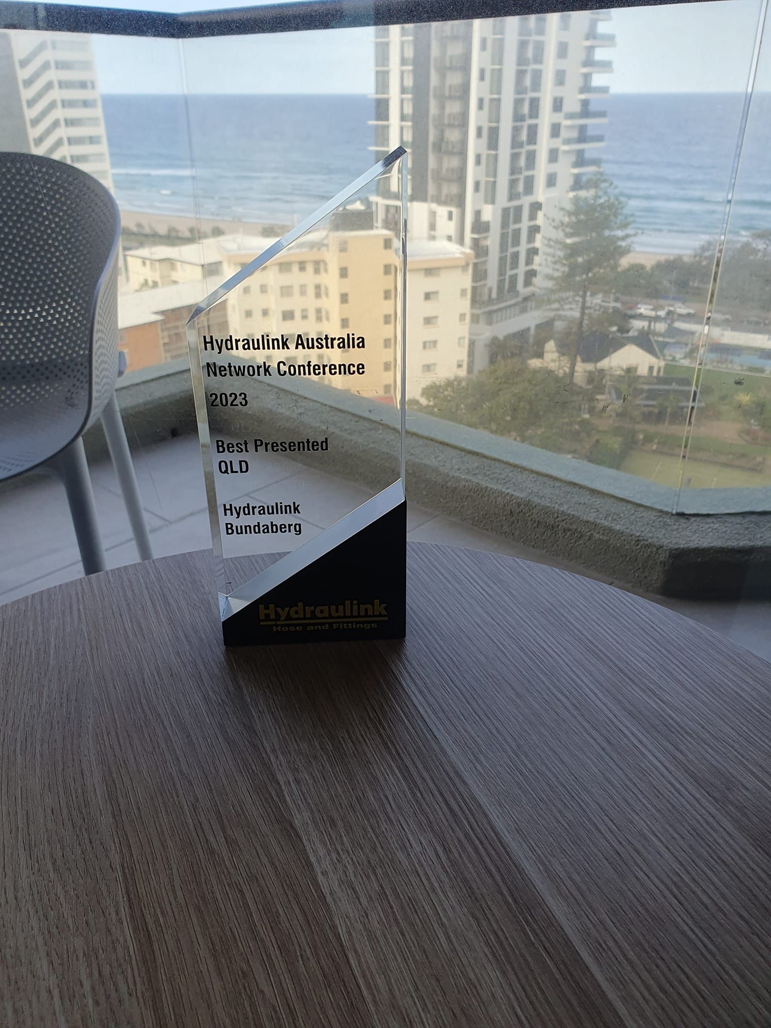 Clear acrylic sign on a carpeted balcony table overlooking ocean and high-rise buildings.
