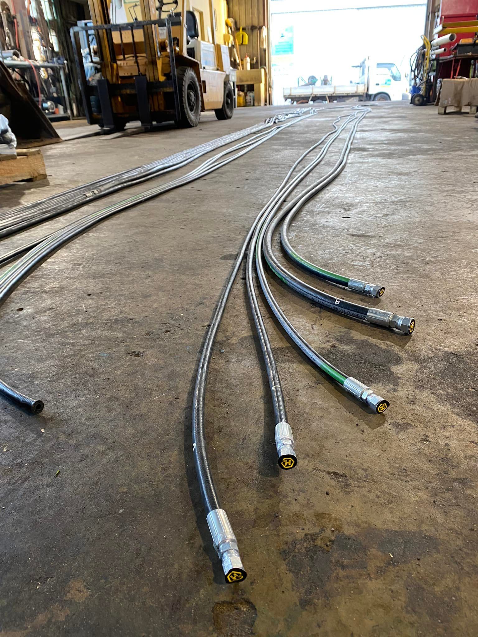 Coiled metal hoses laid across a warehouse floor, with machinery and shelves in the background