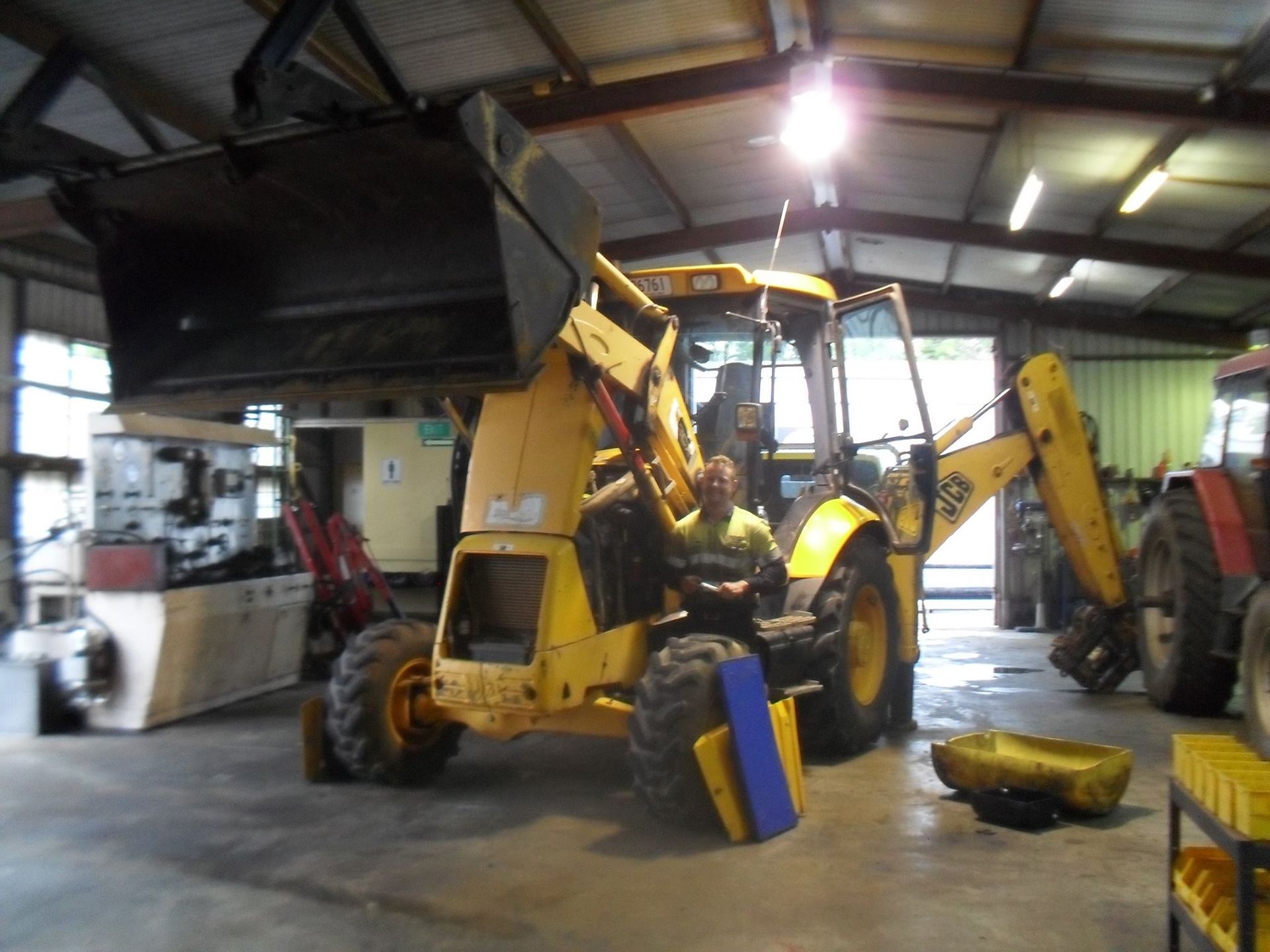 Yellow backhoe loader inside a workshop, with tools and equipment nearby.