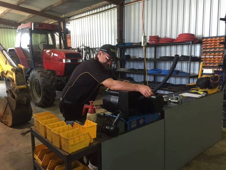 Man working at a bench in a workshop beside a red tractor and tool shelves