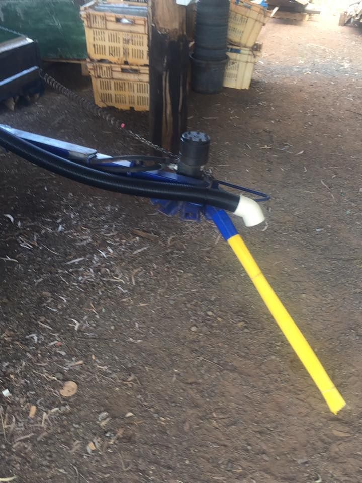 Blue forklift fork near yellow line on dirt ground beside stacked crates and a barrel
