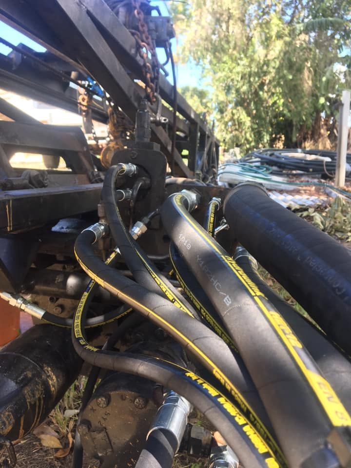 Close-up of tangled black hydraulic hoses and metal machinery outdoors in daylight