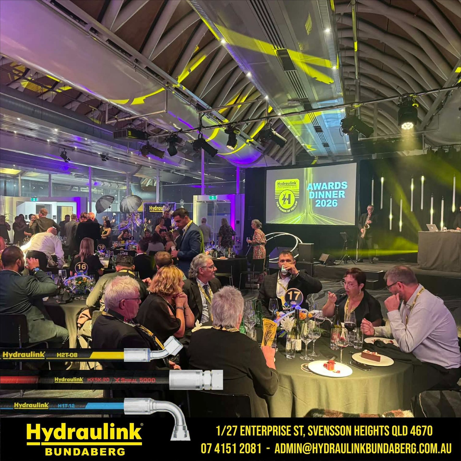 Award dinner in a lit event hall, with guests seated at tables and a stage showing awards graphics.