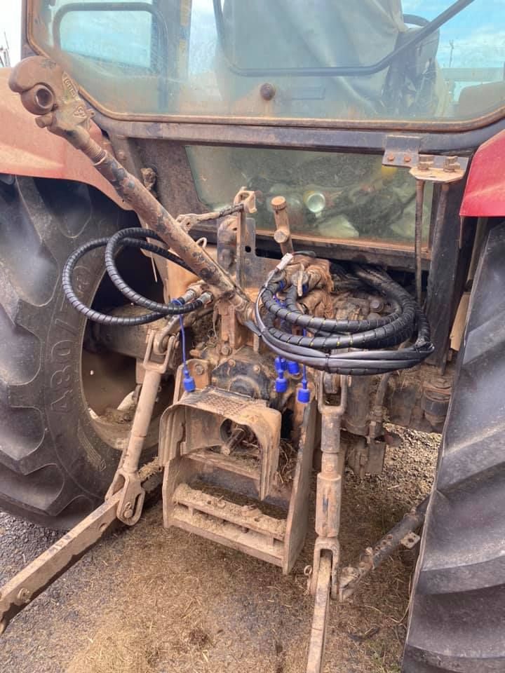 Dirty tractor cab with tangled hoses and a worn control area, seen from the rear.
