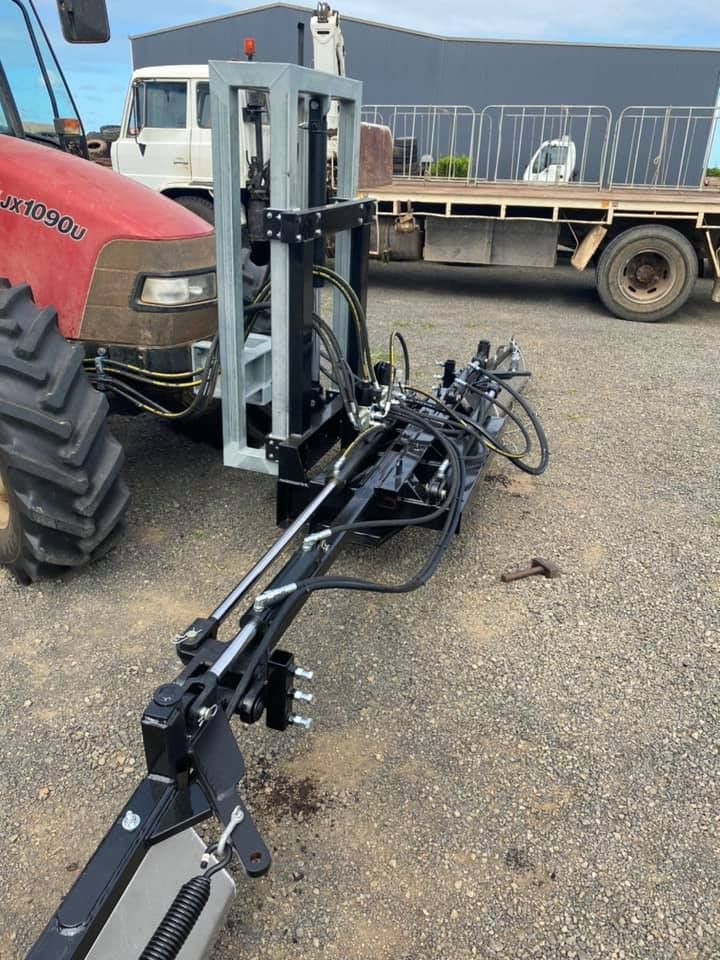 Farm field equipment hitch and hydraulic arm attached to a red tractor in a gravel lot