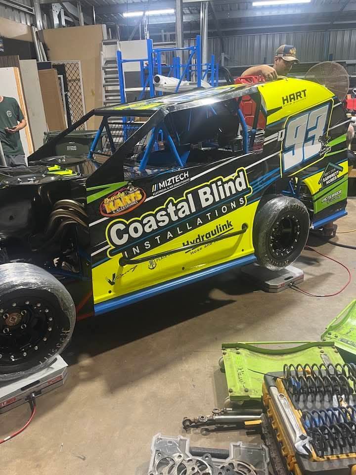 Black and yellow Coastal Bling race car in a garage, with tools and parts on the floor
