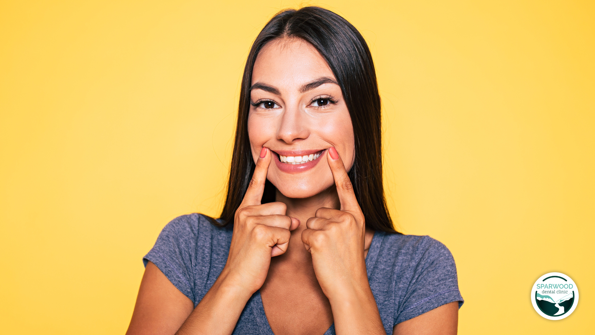 Woman pointing to her smile, against a yellow backdrop.
