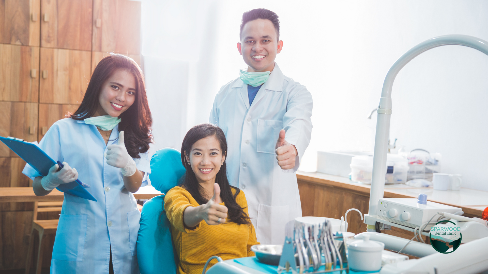 A dentist and a nurse are giving a thumbs up to a patient in a dental chair.