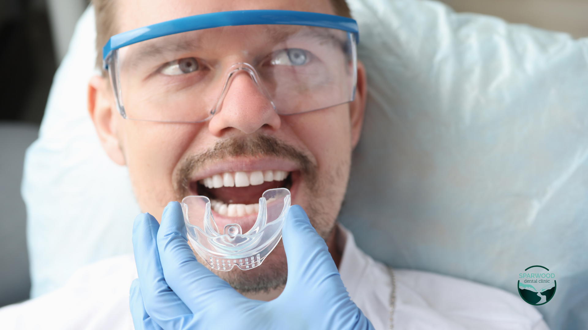 A man wearing glasses and gloves is holding a mouth guard in his mouth.