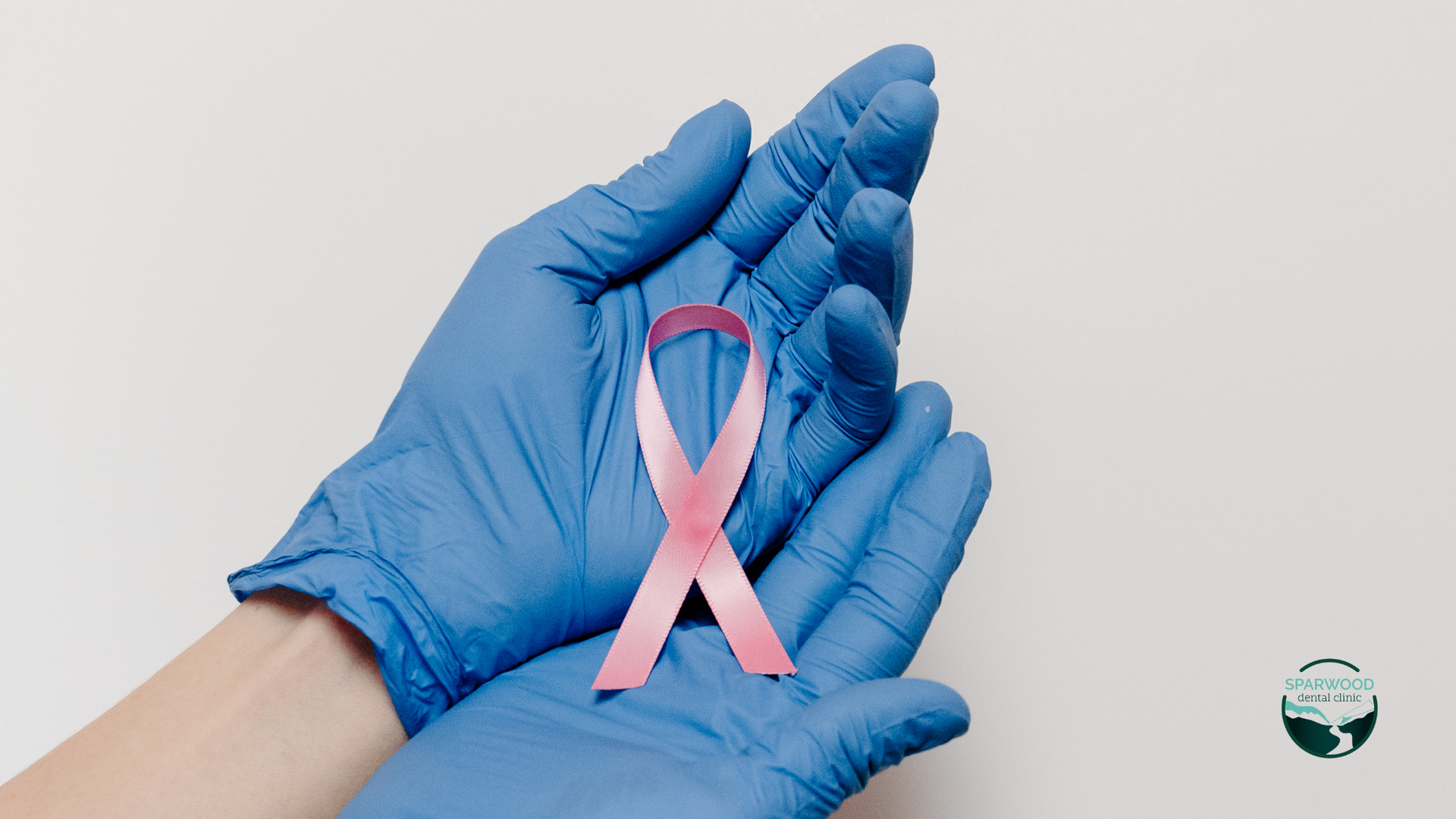 A person wearing blue gloves is holding a pink ribbon.