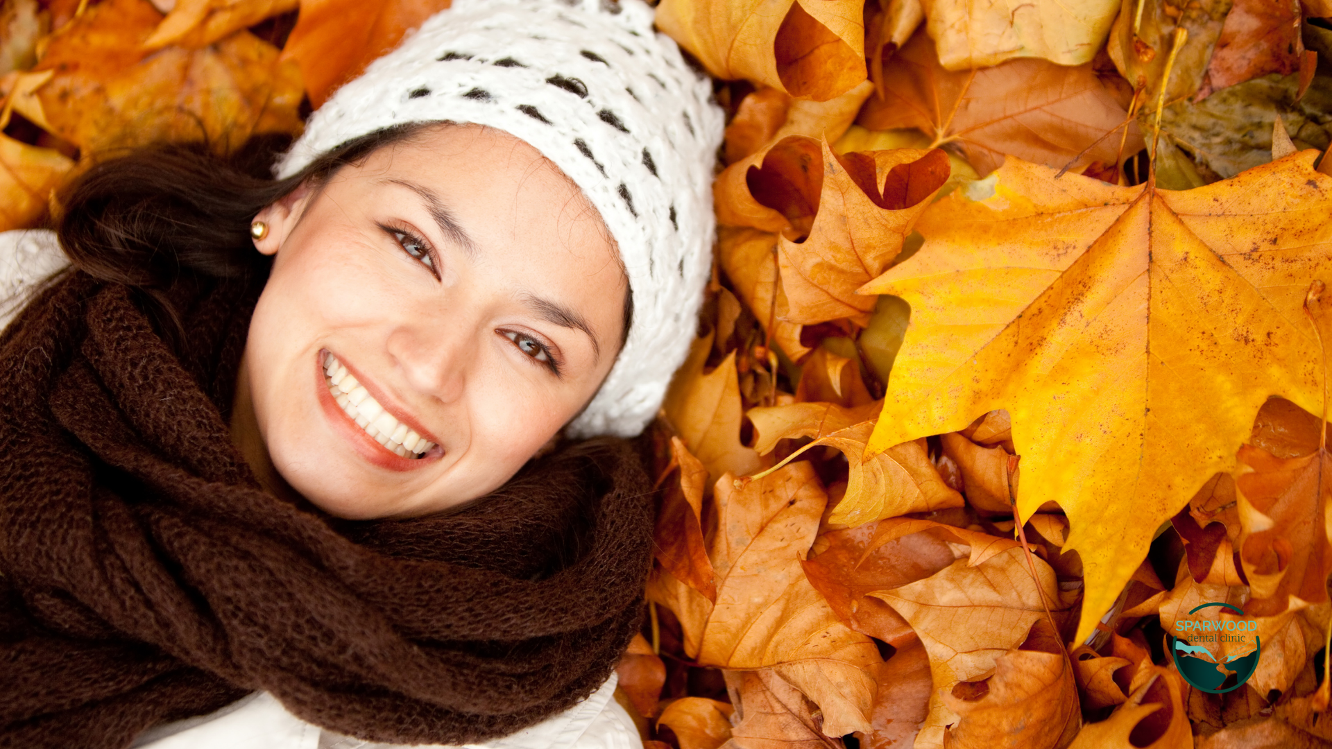 A woman is laying on a pile of leaves and smiling.