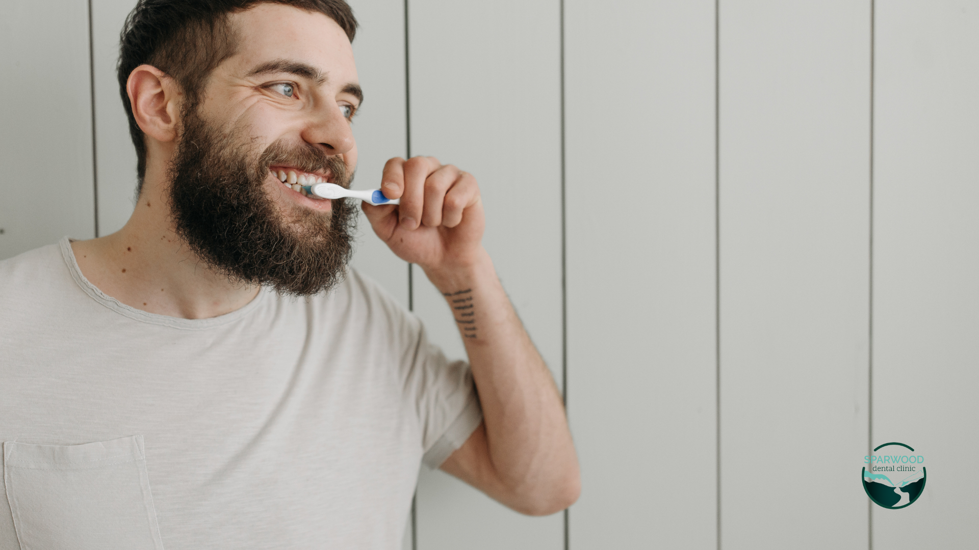 A man with a beard is brushing his teeth in a bathroom.
