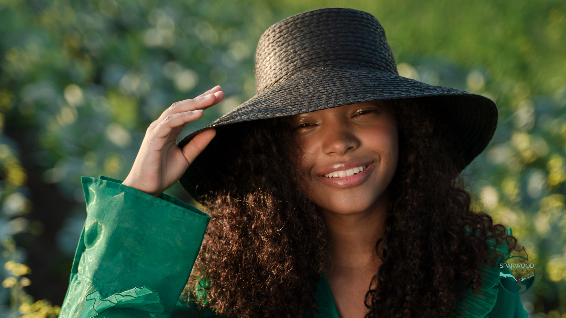 A woman wearing a black hat and a green jacket is smiling.