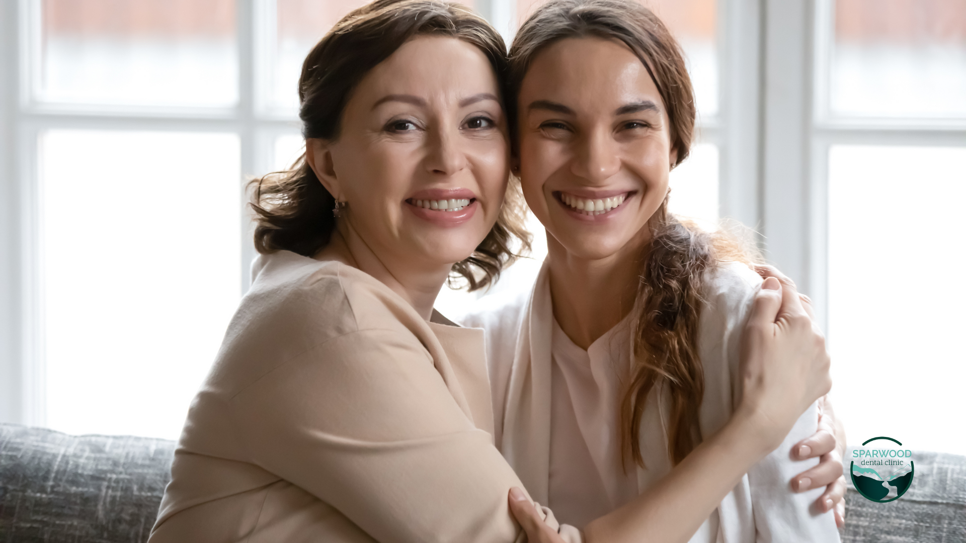 Two women are hugging each other while sitting on a couch.