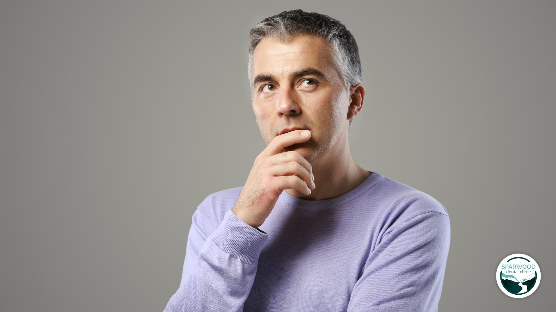 A man in a purple sweater is thinking with his hand on his chin.