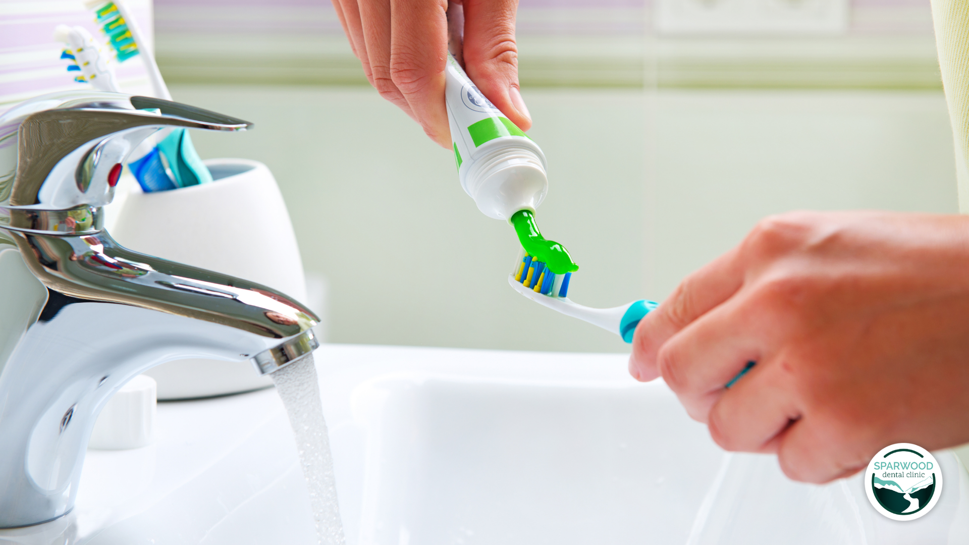 Person squeezing green toothpaste onto a toothbrush in a bathroom with running water.