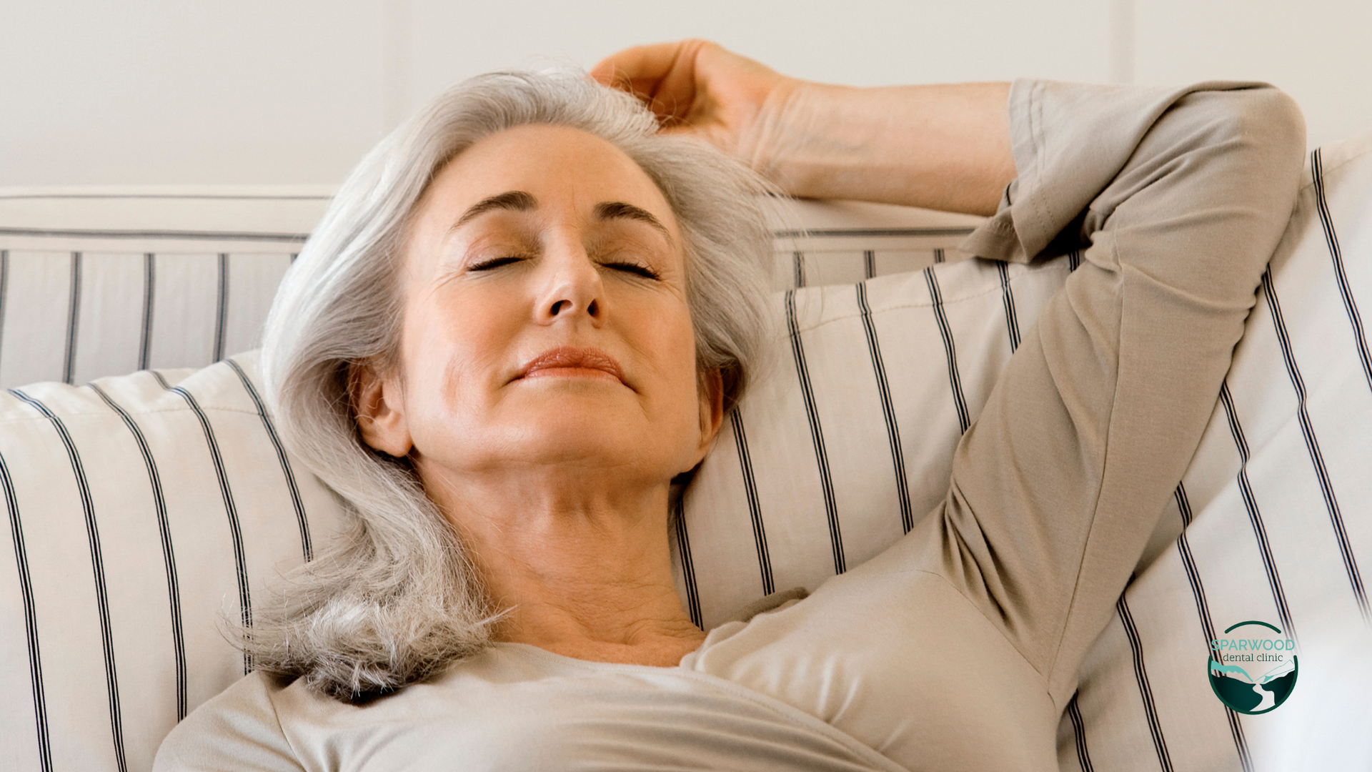 An older woman is laying on a couch with her eyes closed.