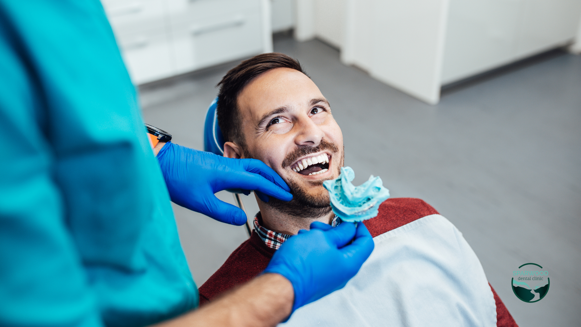 A man is sitting in a dental chair while a dentist examines his teeth.