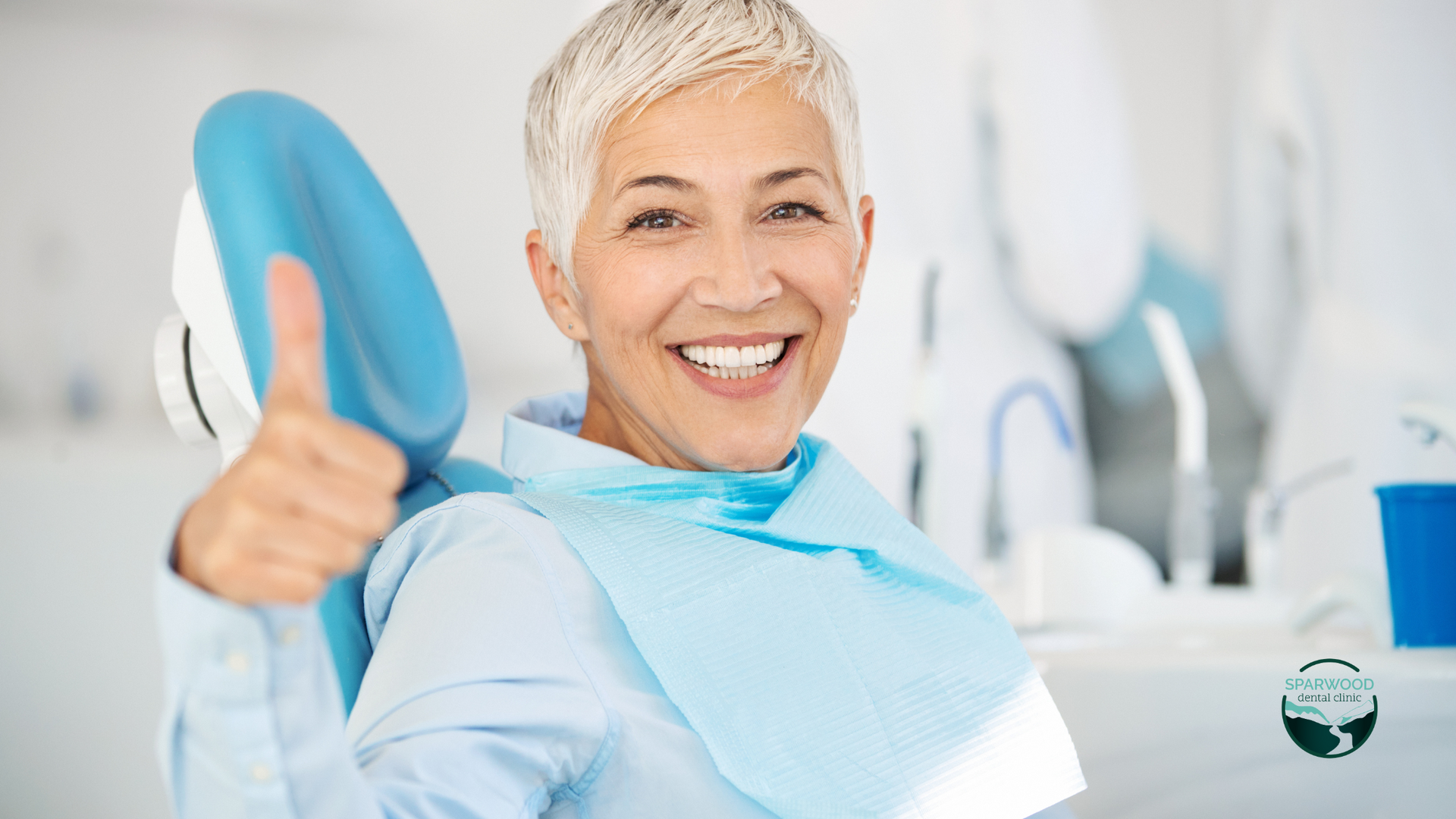 A woman is sitting in a dental chair and giving a thumbs up.