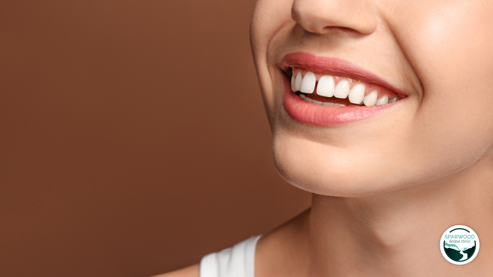 A close up of a woman 's smile with a brown background.
