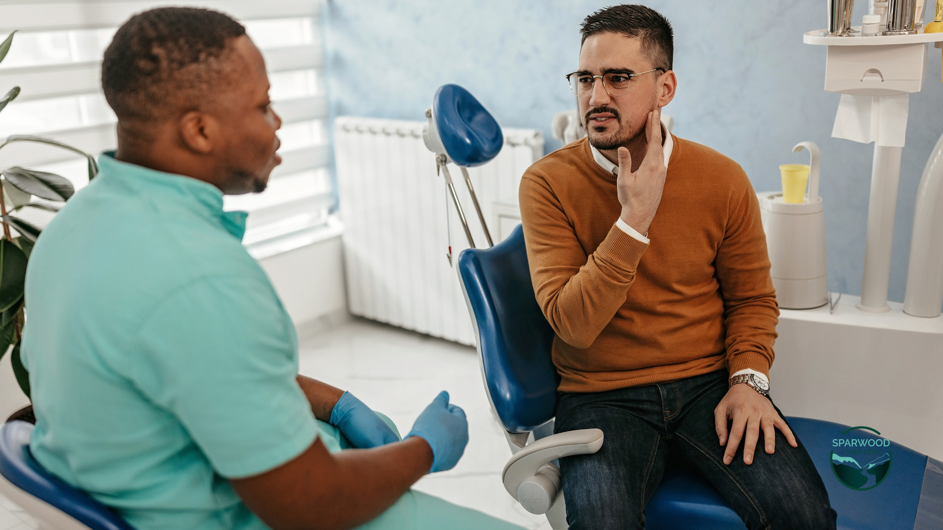 A man is sitting in a dental chair talking to a dentist.