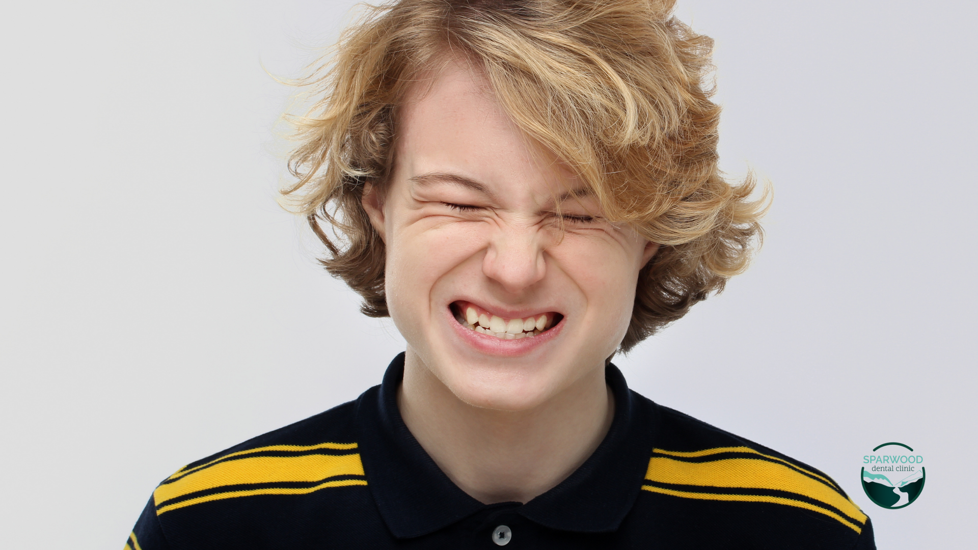 A young man with blonde hair is making a funny face with his eyes closed.