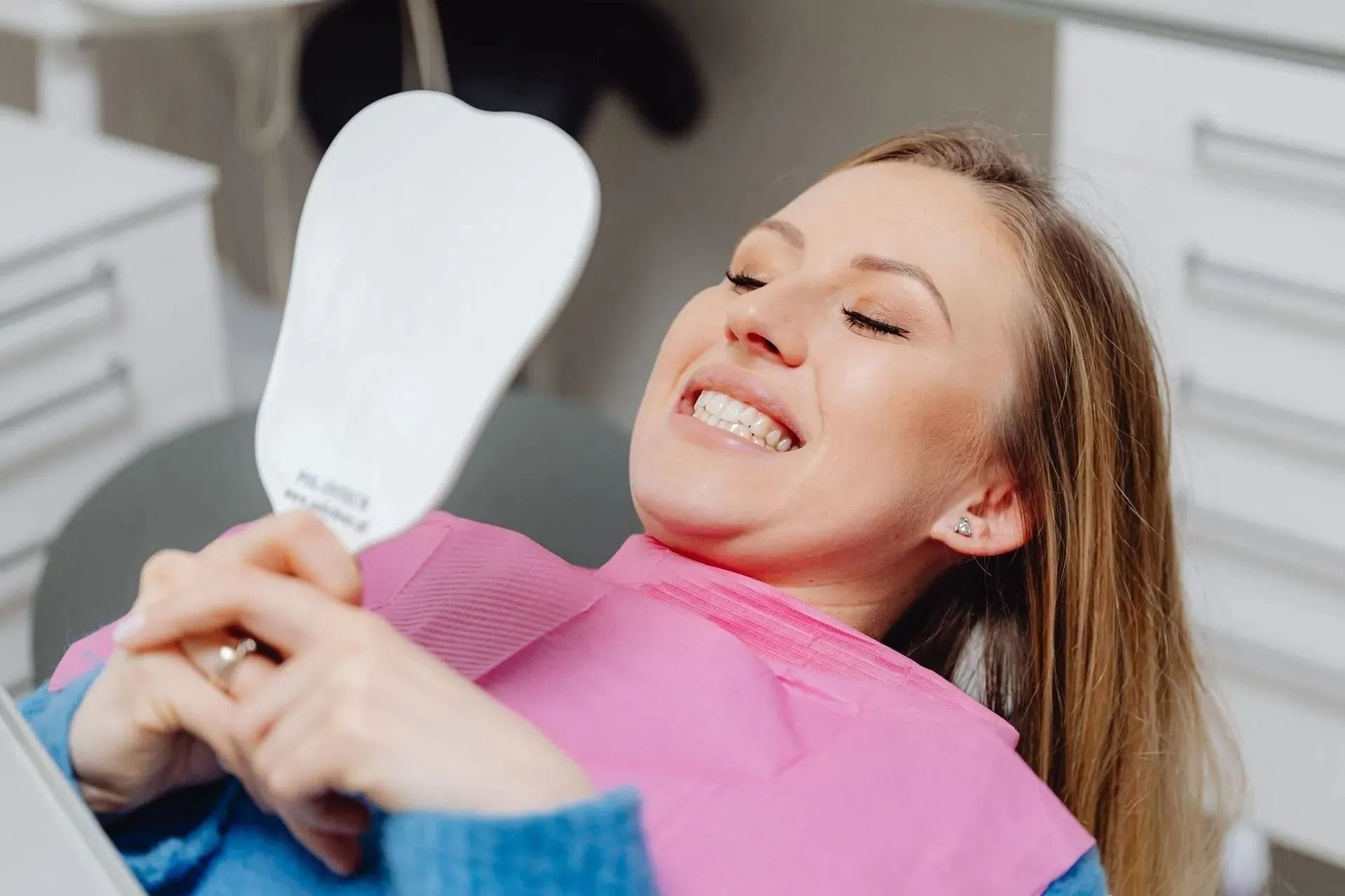 Woman smiling in a dental chair holding a mirror, with a dentist in blue gloves nearby