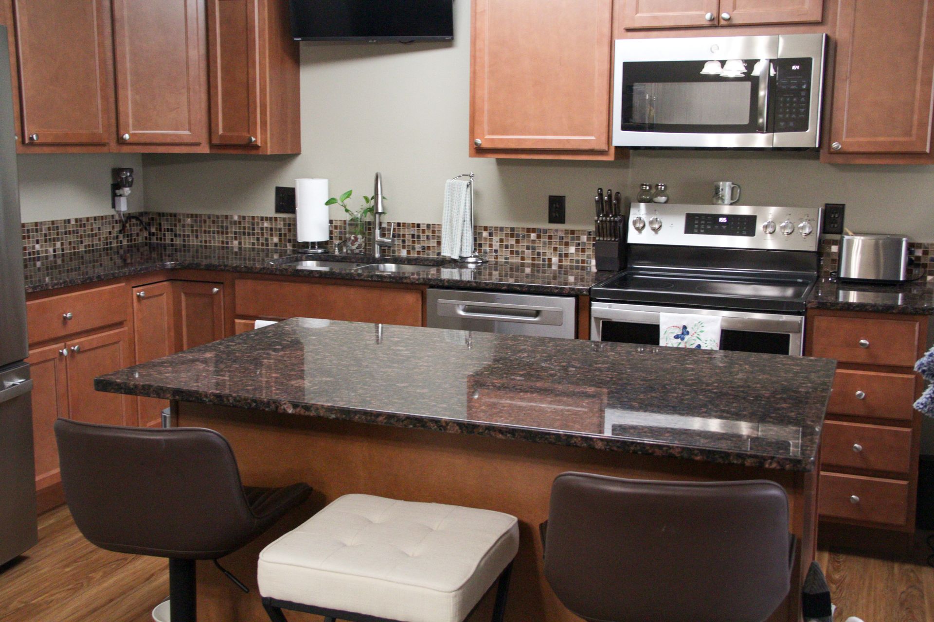 Kitchen with brown cabinets, granite countertops, stainless steel appliances, and a breakfast bar with stools.