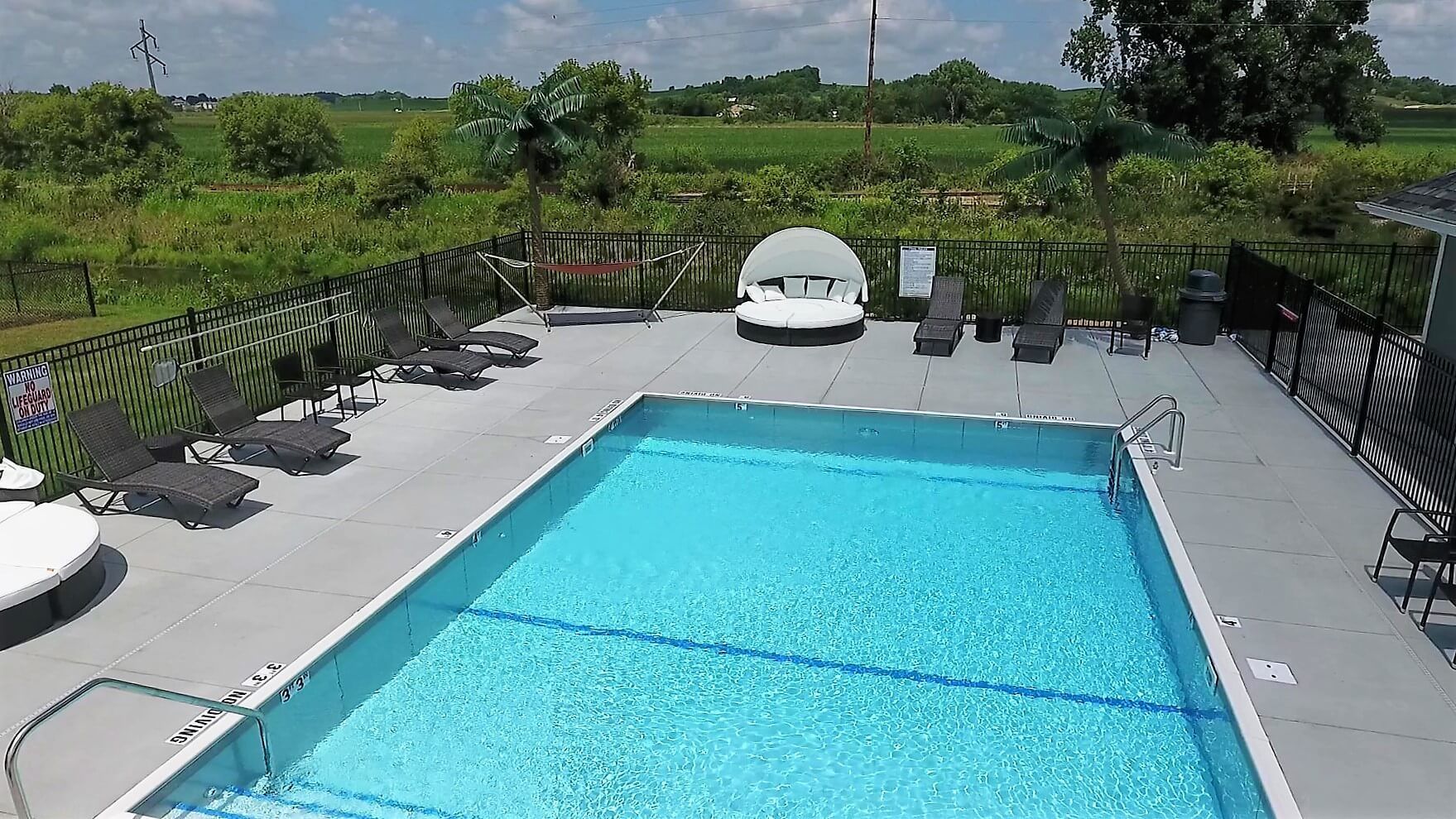 Swimming pool with lounge chairs on a deck, surrounded by greenery.