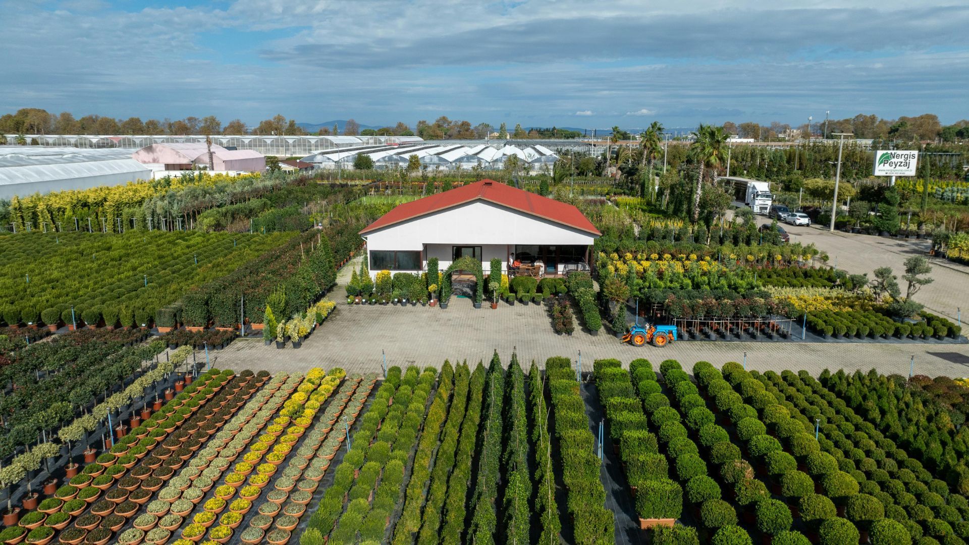 Aerial view of a plant nursery with rows of potted plants and a small red-roofed building center frame