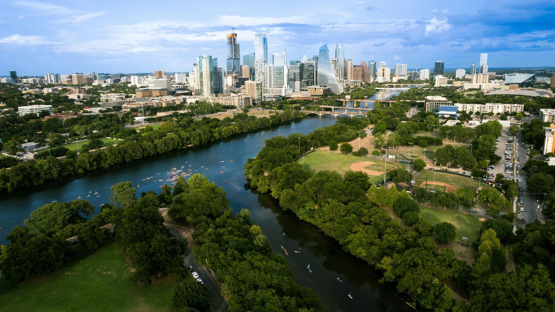 Wide river winding past a green park toward a distant city skyline under a bright blue sky