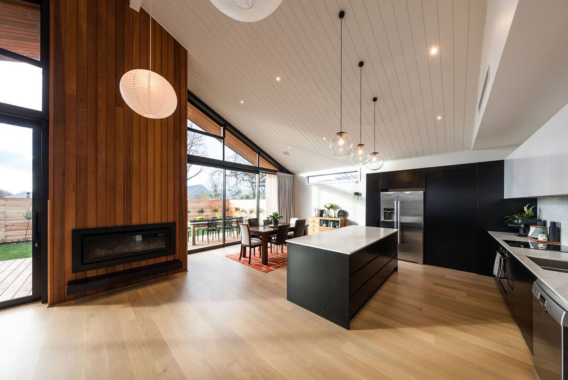 Modern open-plan kitchen and living room with wood accents, black cabinetry, large windows, and pendant lights
