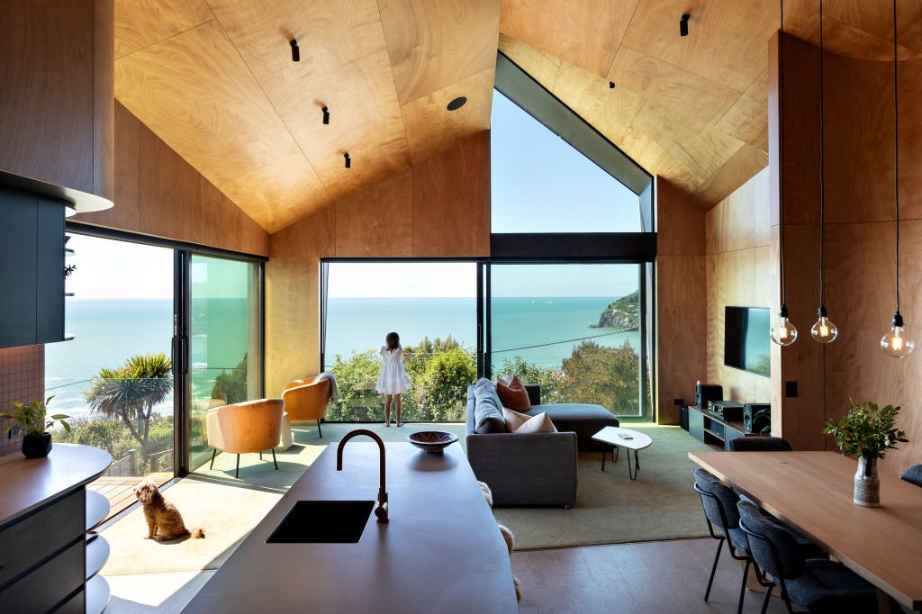 Modern wood-and-glass living room with panoramic ocean views and a central kitchen island