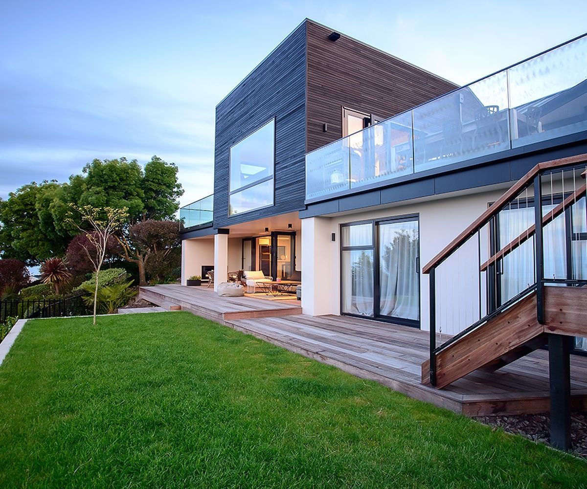 Modern house with large windows, balcony, and green lawn at dusk