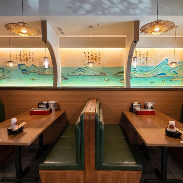 Empty restaurant booth with green vinyl seats, wooden tables, and a sea-themed mural lit by warm pendant lights