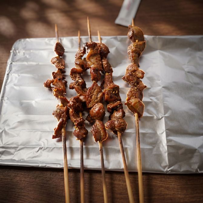 Grilled meat skewers on a foil-lined tray atop a wooden table