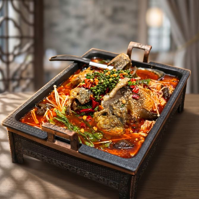 Spicy braised meat in a square cast-iron pot, garnished with peppers and herbs on a table